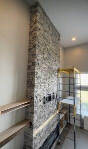 An 8-foot fireplace wall built with faux stacked stone, custom white shaker cabinets, oak floating shelves, and a Touchstone electric fireplace. See how Radford Woodworks built a full-height focal point that transformed this Indiana living room.