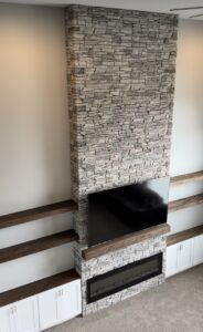 An 8-foot fireplace wall built with faux stacked stone, custom white shaker cabinets, oak floating shelves, and a Touchstone electric fireplace. See how Radford Woodworks built a full-height focal point that transformed this Indiana living room.