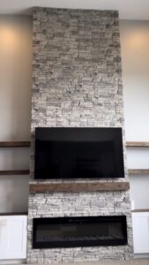 An 8-foot fireplace wall built with faux stacked stone, custom white shaker cabinets, oak floating shelves, and a Touchstone electric fireplace. See how Radford Woodworks built a full-height focal point that transformed this Indiana living room.
