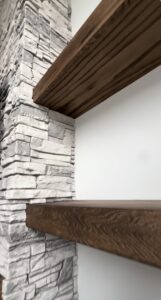 An 8-foot fireplace wall built with faux stacked stone, custom white shaker cabinets, oak floating shelves, and a Touchstone electric fireplace. See how Radford Woodworks built a full-height focal point that transformed this Indiana living room.