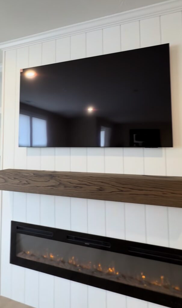 A behind-the-scenes look at a custom fireplace build-out in Westfield, Indiana — vertical shiplap, deep storage cabinets, a dark oak mantle, and a factory-level finish sprayed on-site. See why process drives the final result.