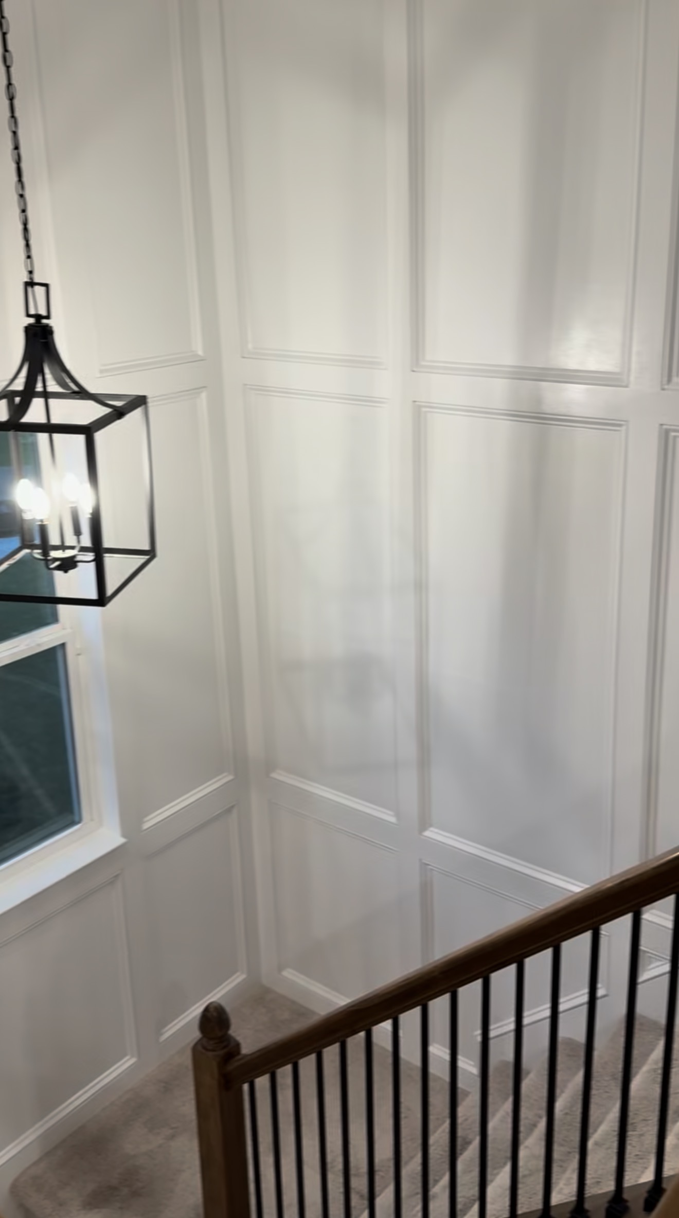 Stairwell trim carpentry can turn a blank wall into a lasting feature with a custom grid layout, inset base cap molding, traditional profiles, and a clean painted finish.