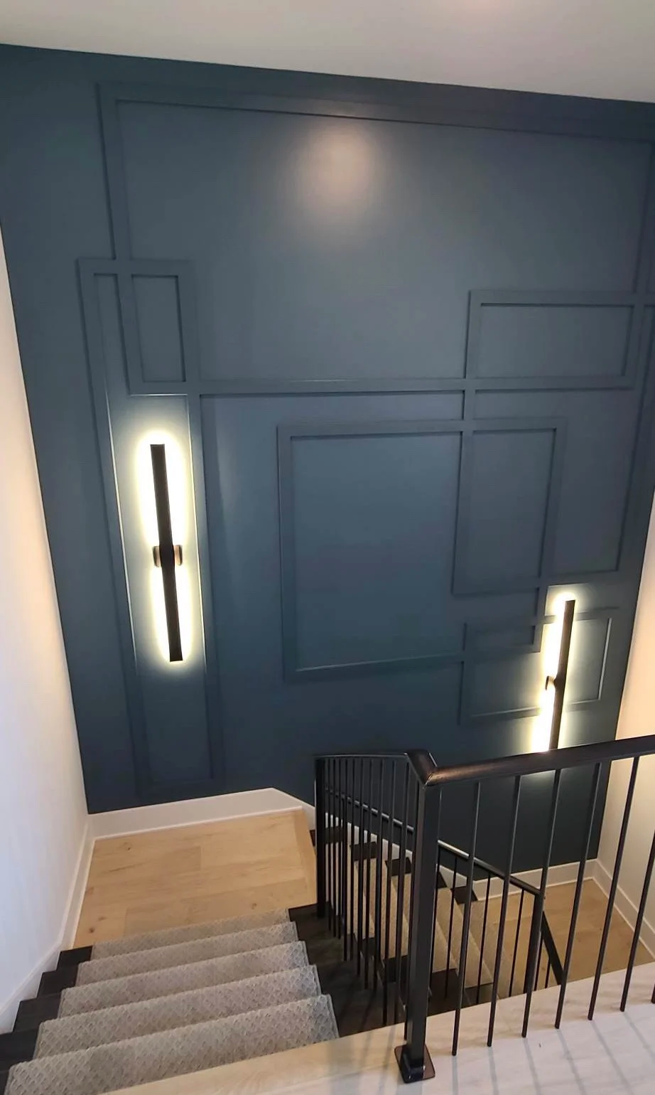 Navy geometric trim accent wall running the full height of a stairwell, lit by paired vertical sconces