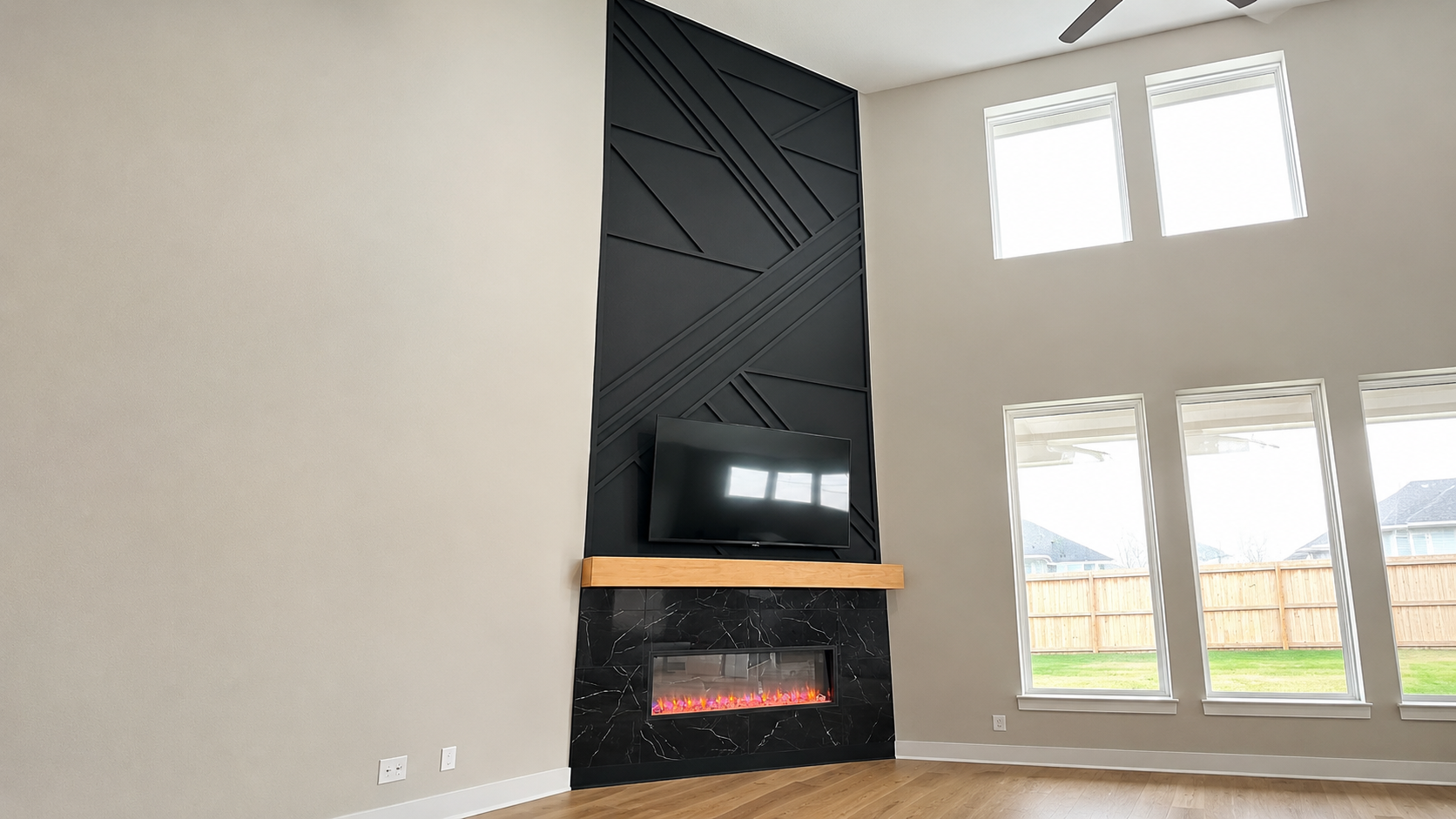 Two-story black geometric trim fireplace wall with marble-look tile surround, floating wood mantel, and recessed linear electric fireplace by Radford Woodworks