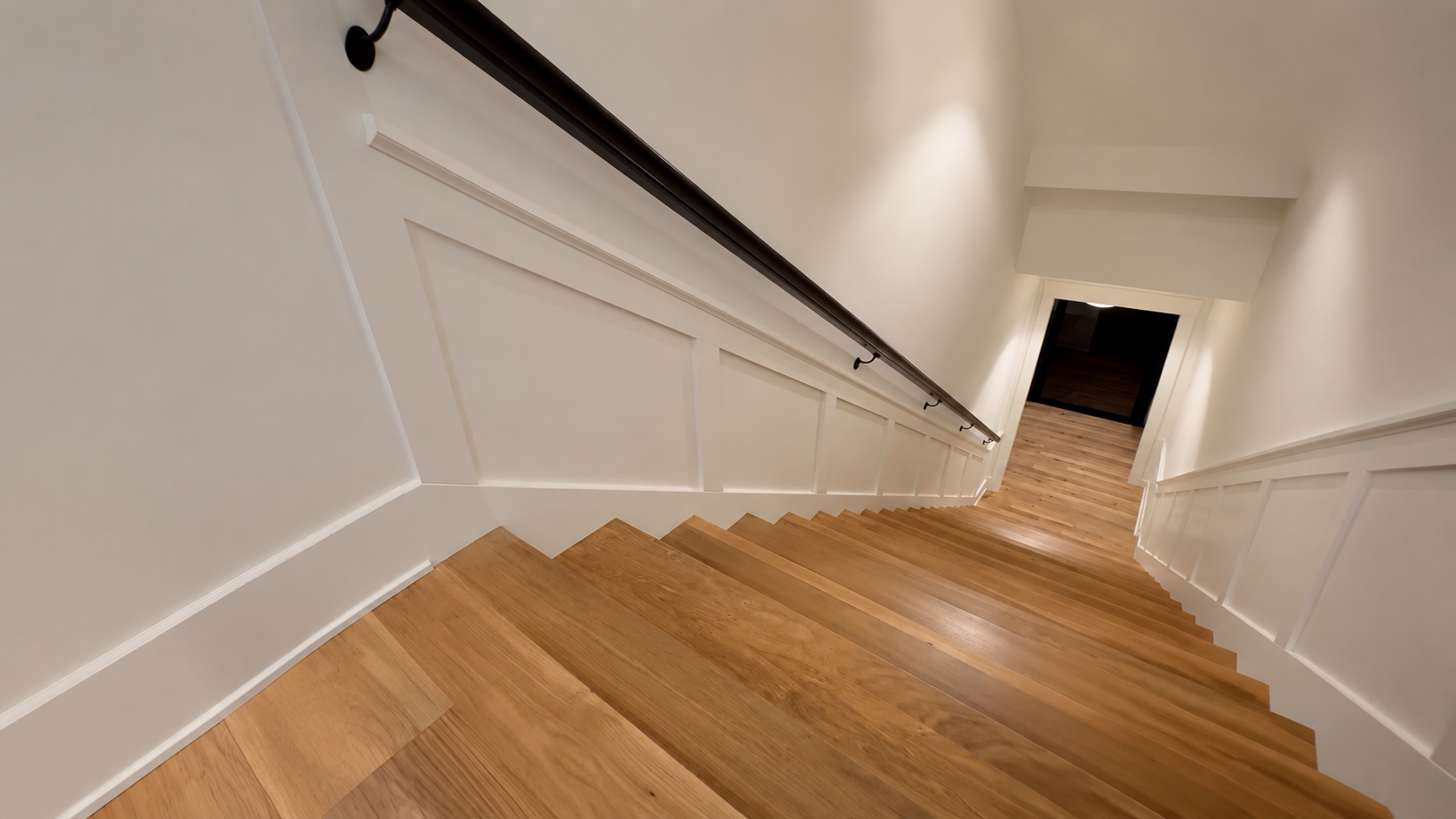 Flat panel stair wainscoting stepping down both walls of an oak staircase with a black metal handrail