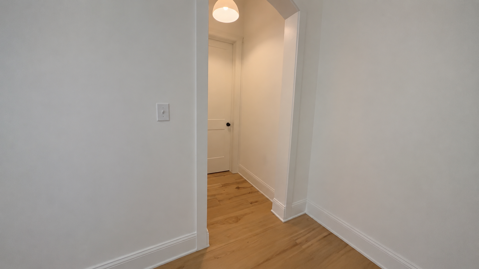 Flat white hallway wall with plain baseboard and an arched opening, no wall paneling yet