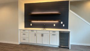 Wet bar vs dry bar example: a Radford Woodworks wet bar with white shaker cabinets, a dark shiplap wall, LED-lit floating shelves, and a glass-front beverage fridge