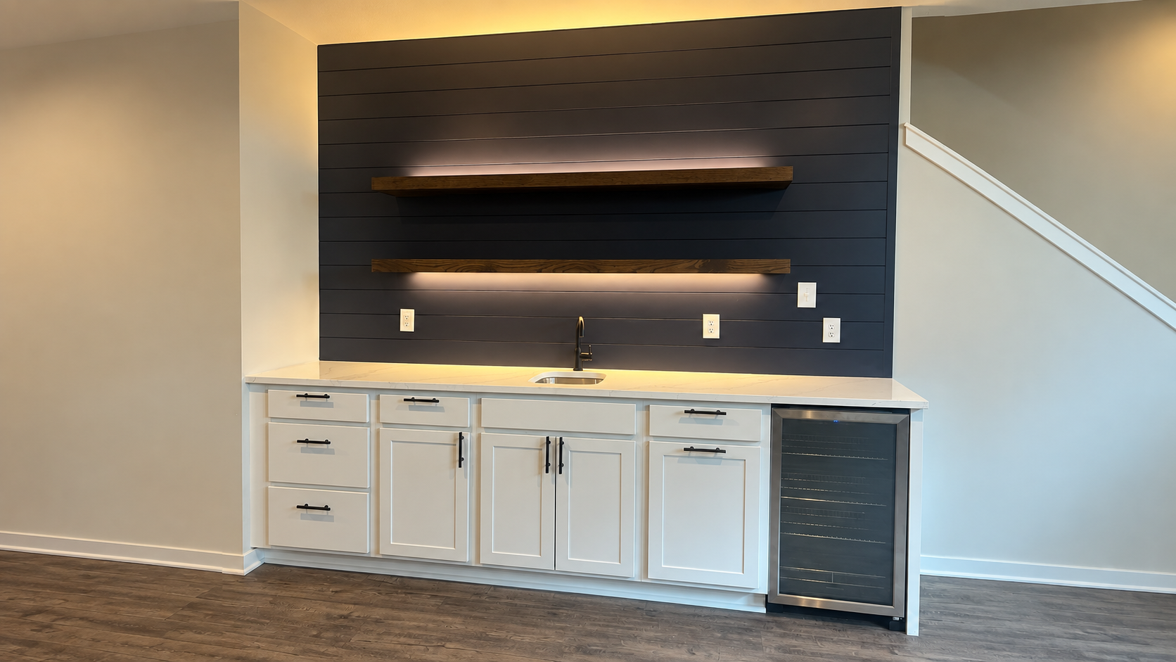 Wet bar vs dry bar example: a Radford Woodworks wet bar with white shaker cabinets, a dark shiplap wall, LED-lit floating shelves, and a glass-front beverage fridge