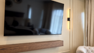 Indiana fluted walls: cream fluted panel framed in trim beside a wall-mounted TV, black sconce, and stained floating shelf